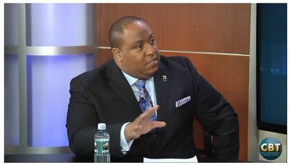 A man in a suit and tie is sitting at a table with a bottle of water