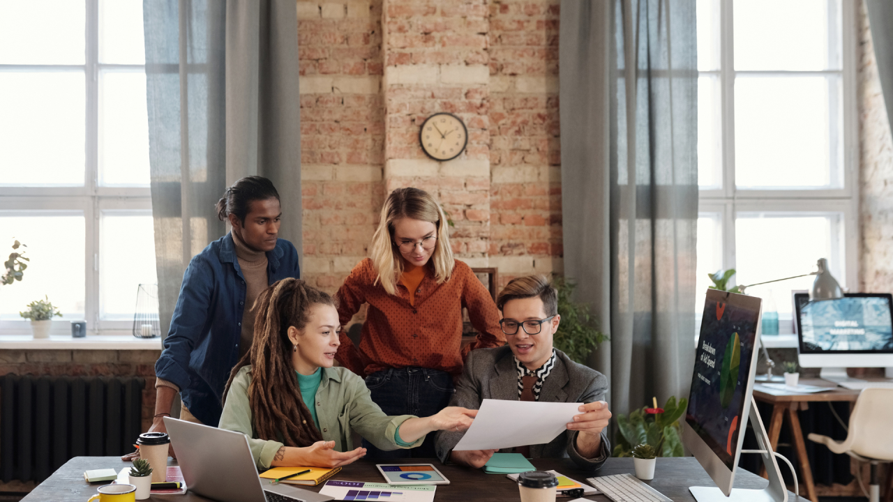 A group of people are sitting around a table in an office looking at a piece of paper.