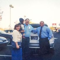 A group of people standing next to a car in a parking lot.