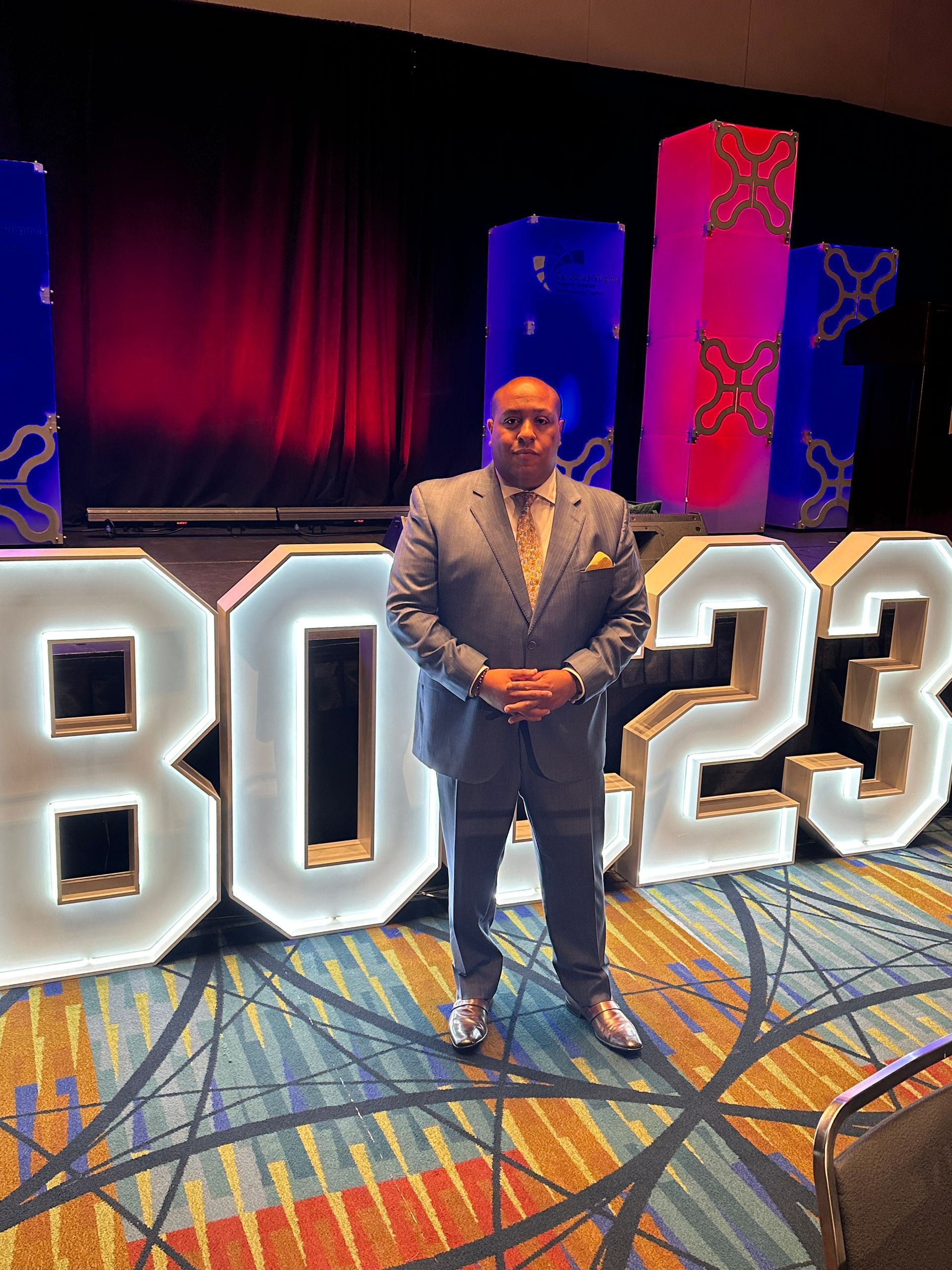 A man in a suit and tie is standing in front of a large sign that says 2023.