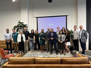 A group of people are posing for a picture in front of a projector screen in a living room.