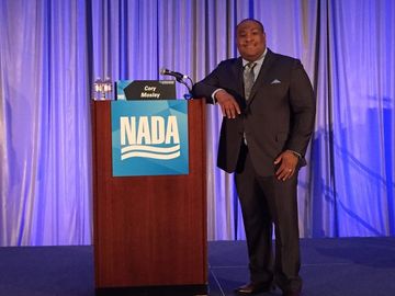 A man in a suit is standing in front of a podium that says nada