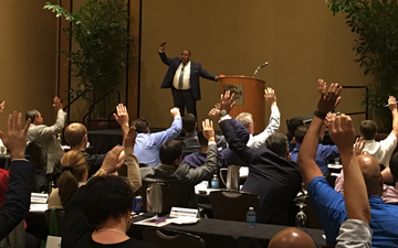 A man is standing in front of a crowd of people with their hands in the air.