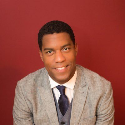 A man in a suit and tie is smiling in front of a red wall.