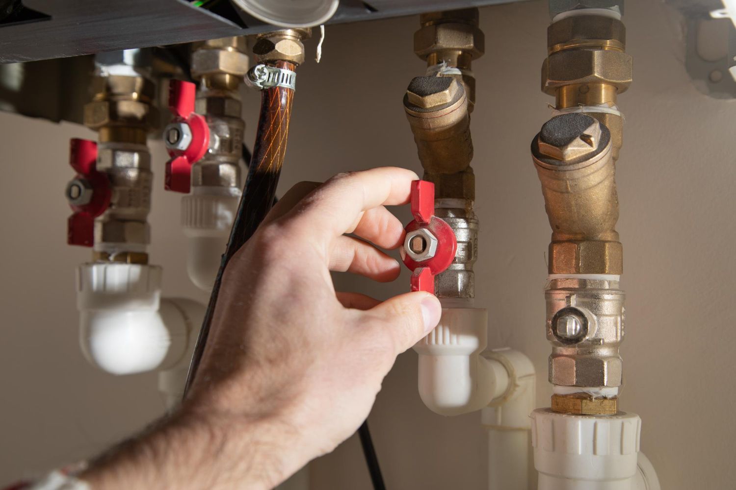 A hand turns a red valve on a brass plumbing pipe system attached to a water heater.