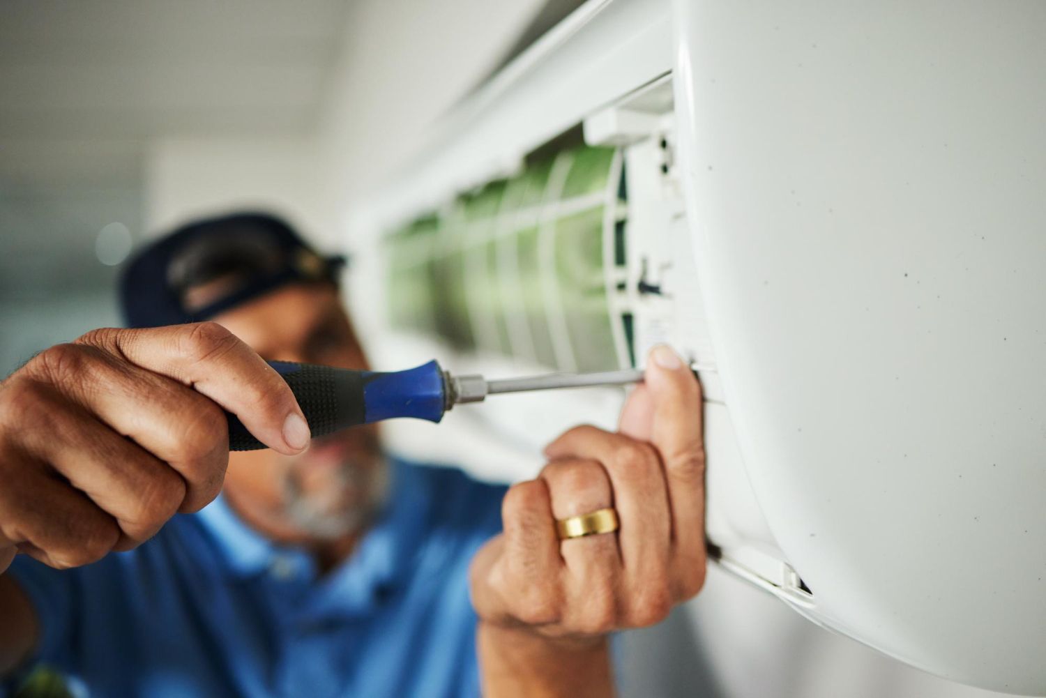 A technician in a blue shirt uses a screwdriver to repair a wall-mounted air conditioning unit.