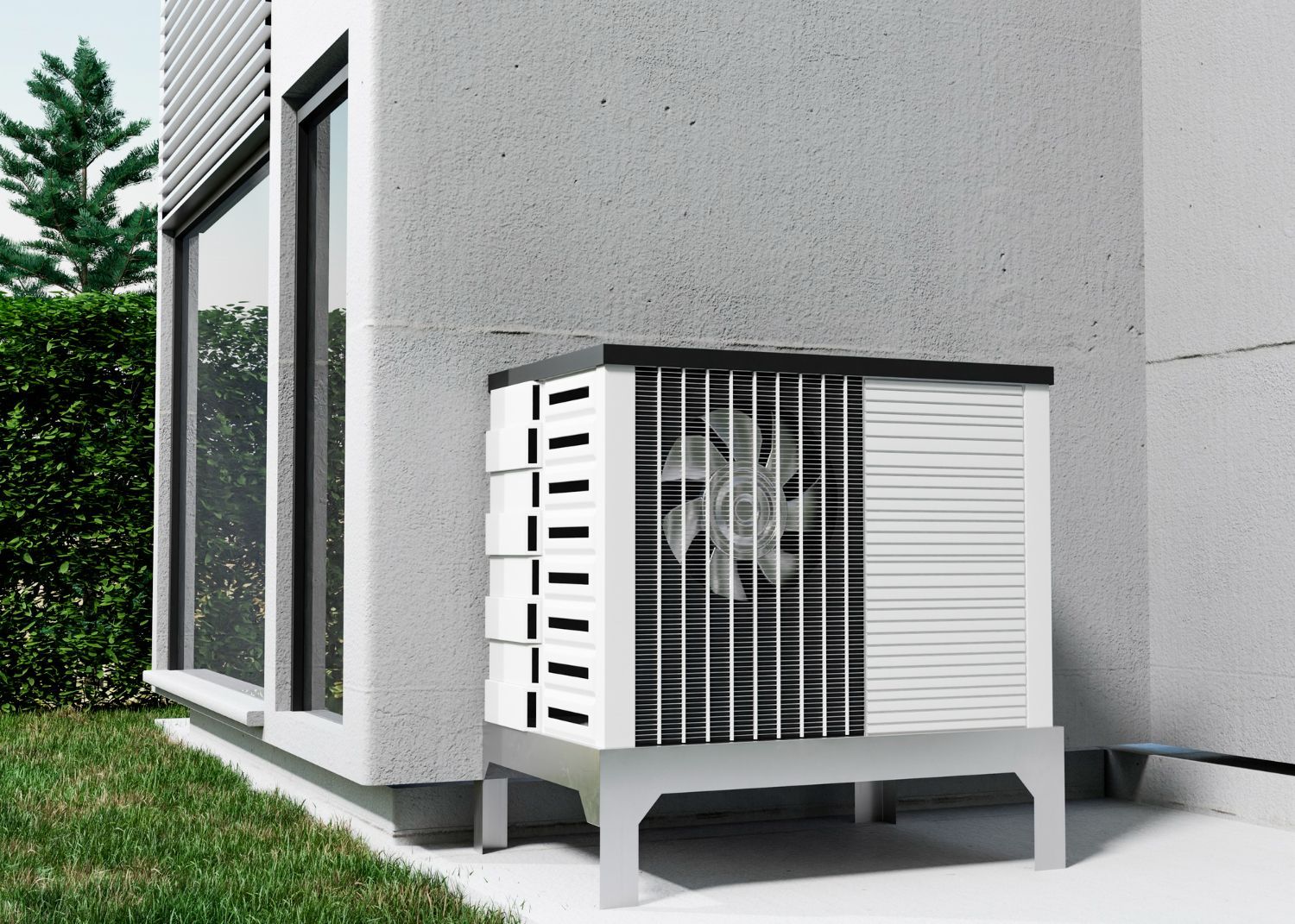 An outdoor heat pump unit sits on a metal stand beside a modern gray concrete building next to a grassy lawn and hedge.