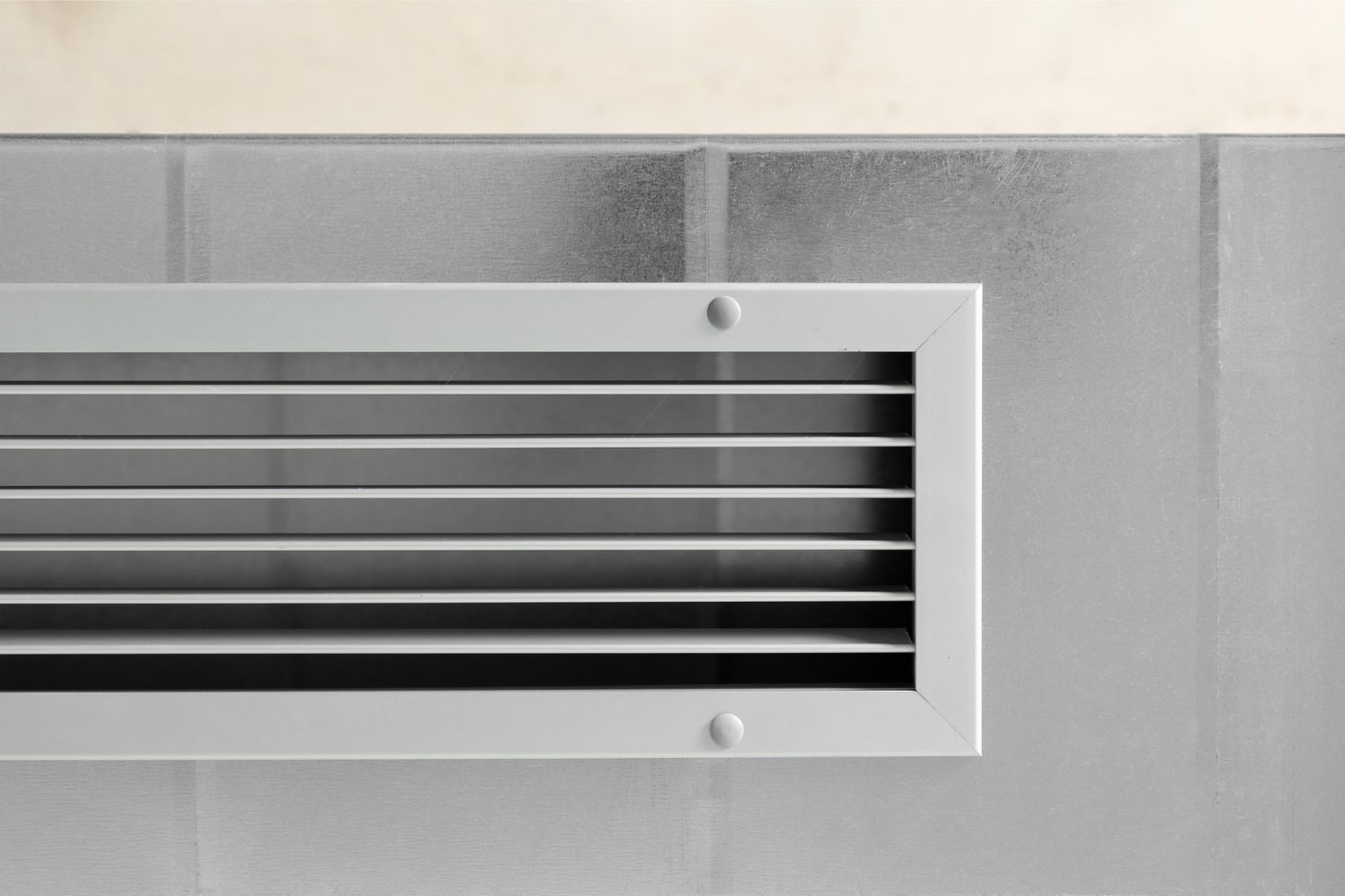A rectangular, horizontal HVAC vent with light gray metal slats, mounted on a brushed metal surface.