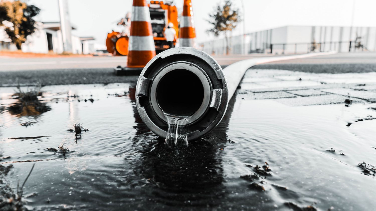 A close-up of an industrial hose nozzle resting on wet pavement with orange traffic cones in the background.