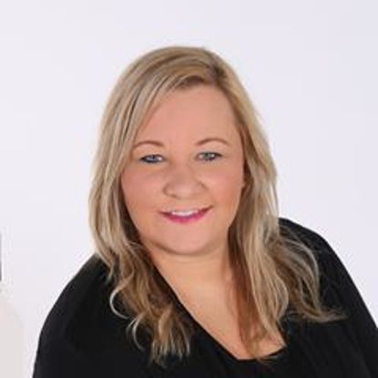 A person with shoulder-length blonde hair and a friendly smile, wearing a black top against a white background.