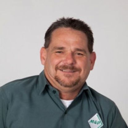 A person wearing a dark green collared shirt with an MGP logo, smiling against a plain white background.