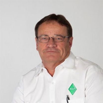A person with short hair and glasses wearing a white collared shirt with a small green logo on the chest.
