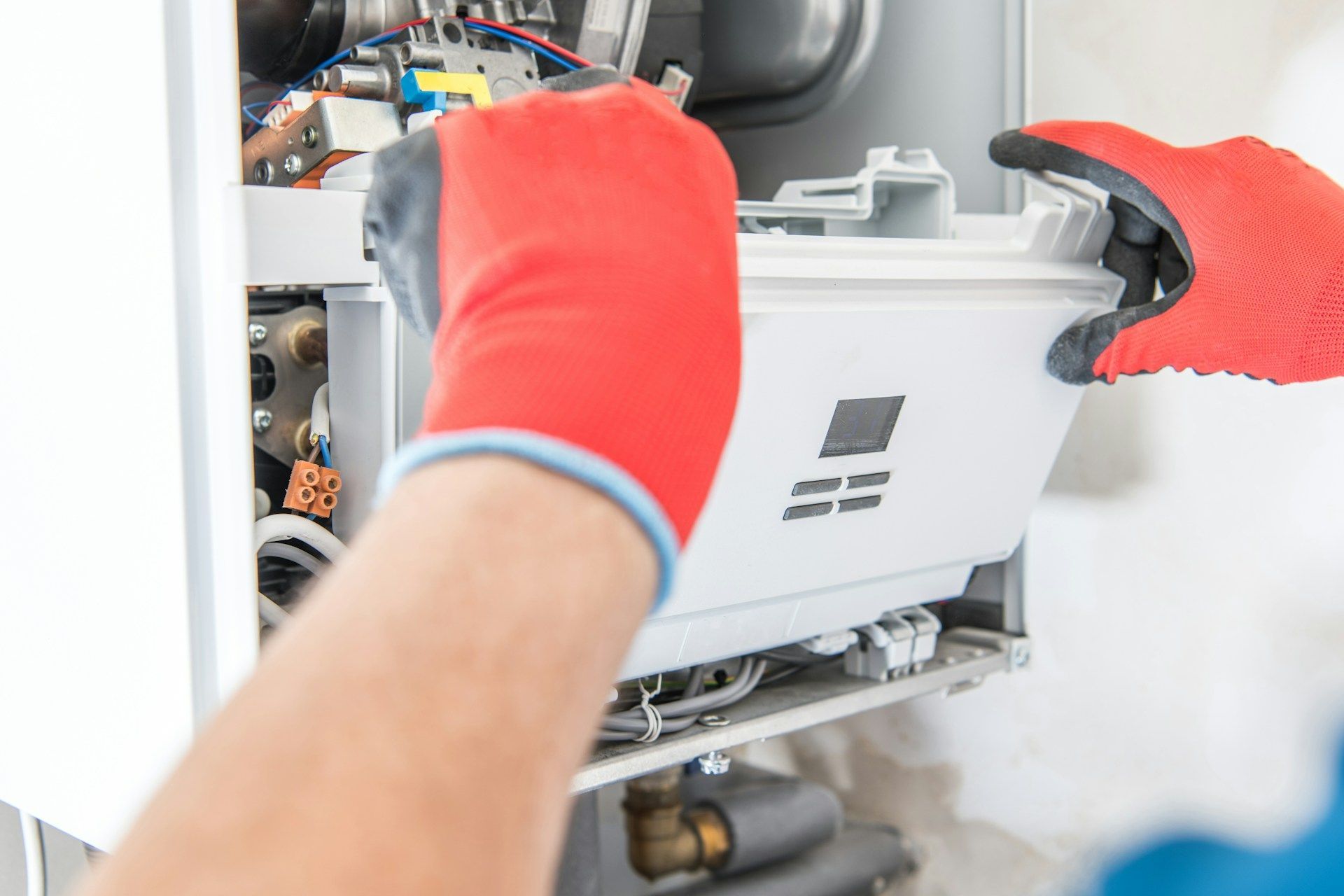 A technician wearing red protective gloves installs or repairs a white heating boiler unit.