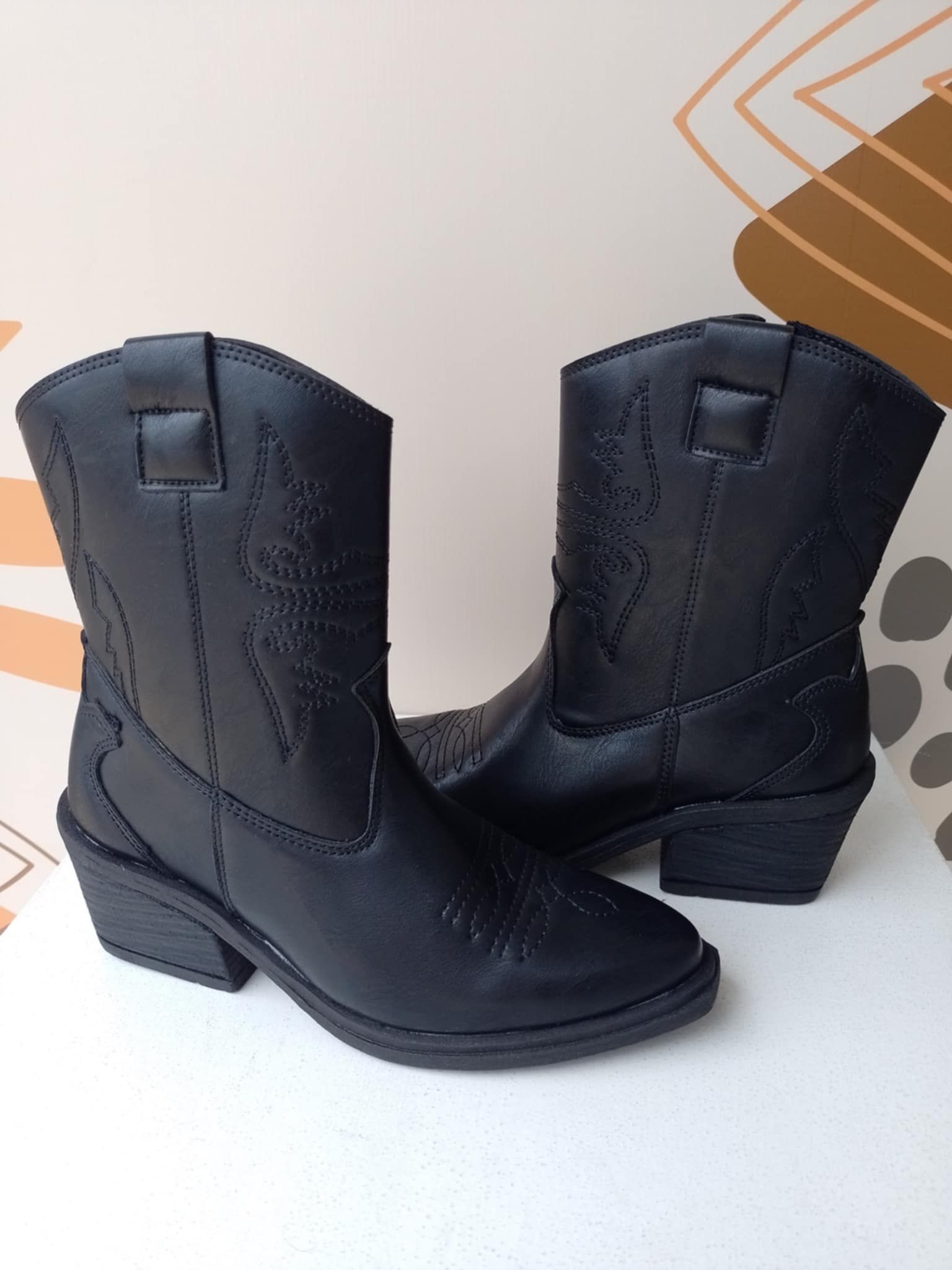 Un par de botas de vaquero negras sobre una superficie blanca.