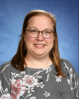 A woman wearing glasses and a floral shirt is smiling for the camera.