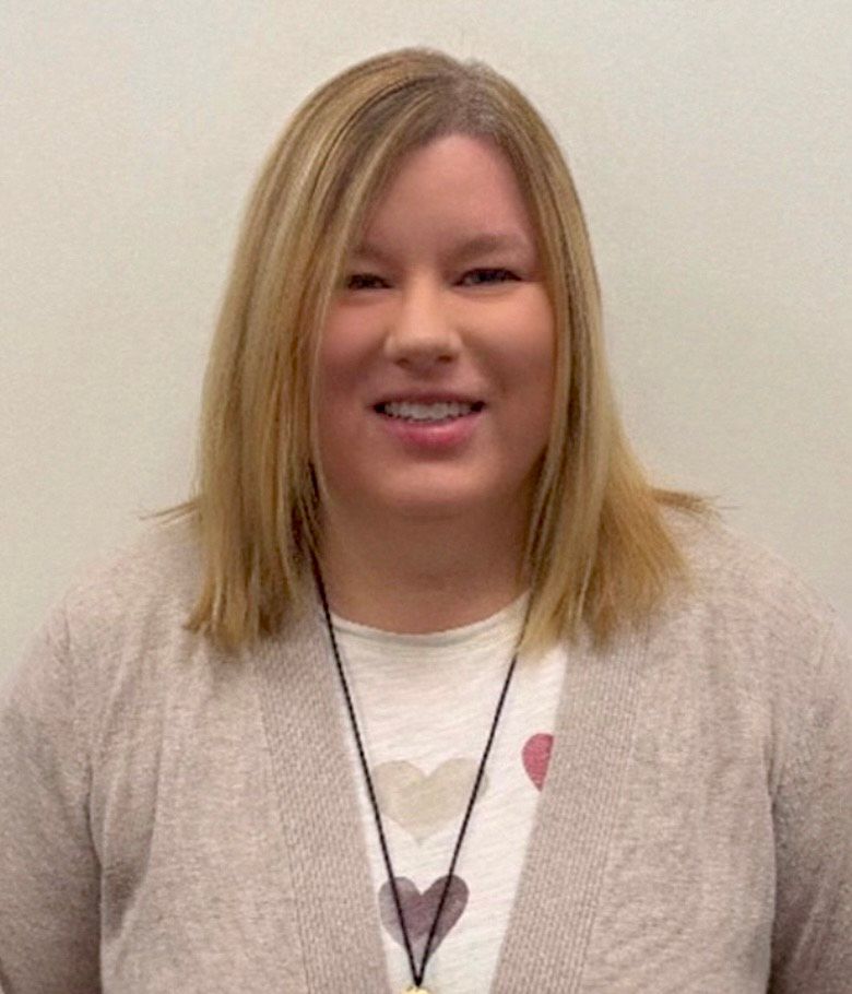 A woman wearing a sweater and a necklace with hearts on it is smiling.