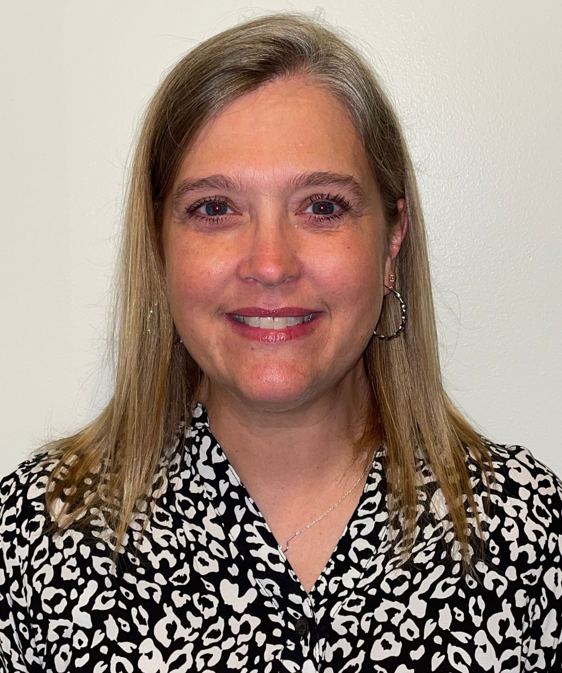 A woman wearing a black and white leopard print shirt is smiling for the camera.