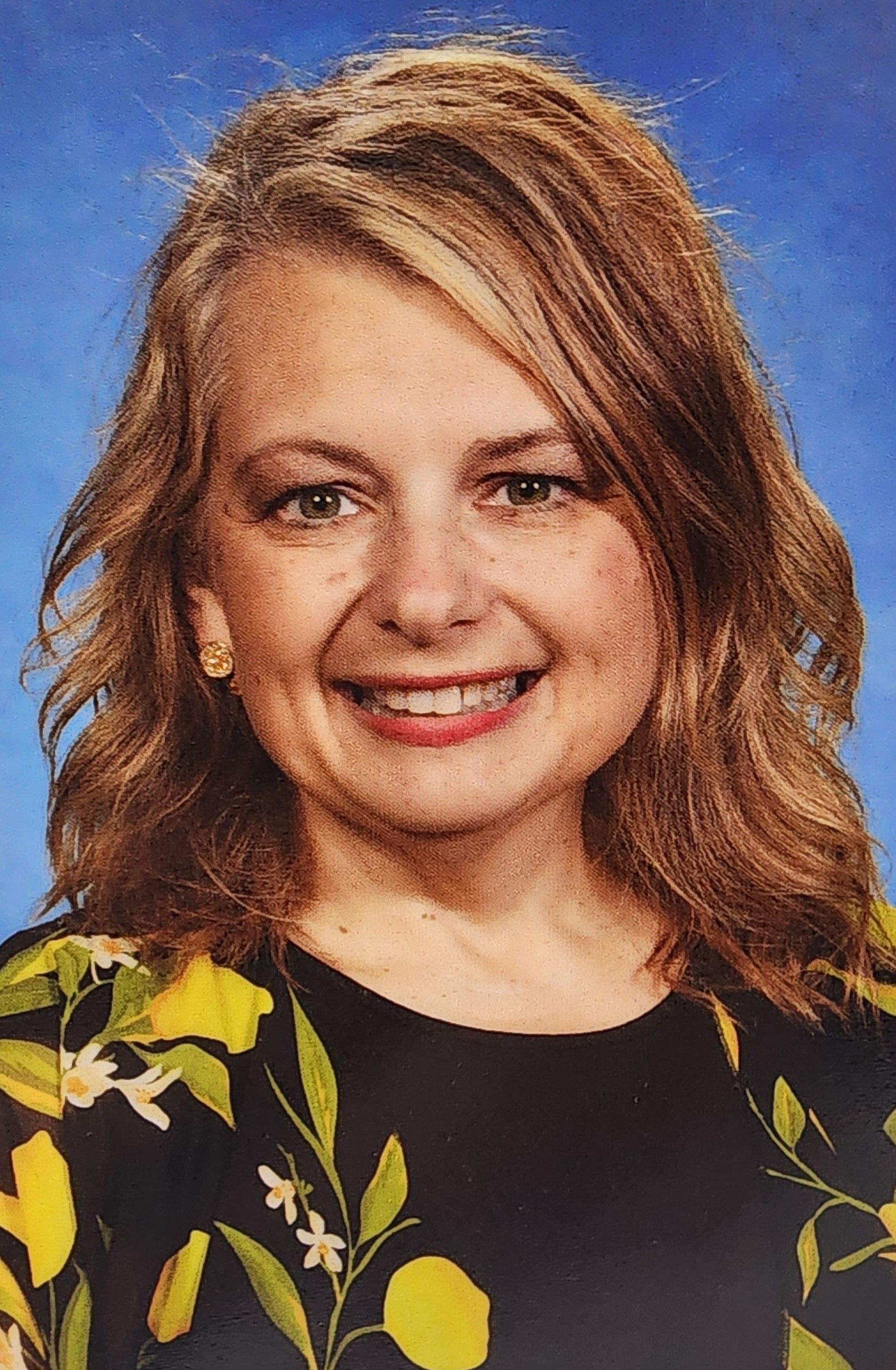 A woman in a black and yellow floral shirt is smiling for the camera.