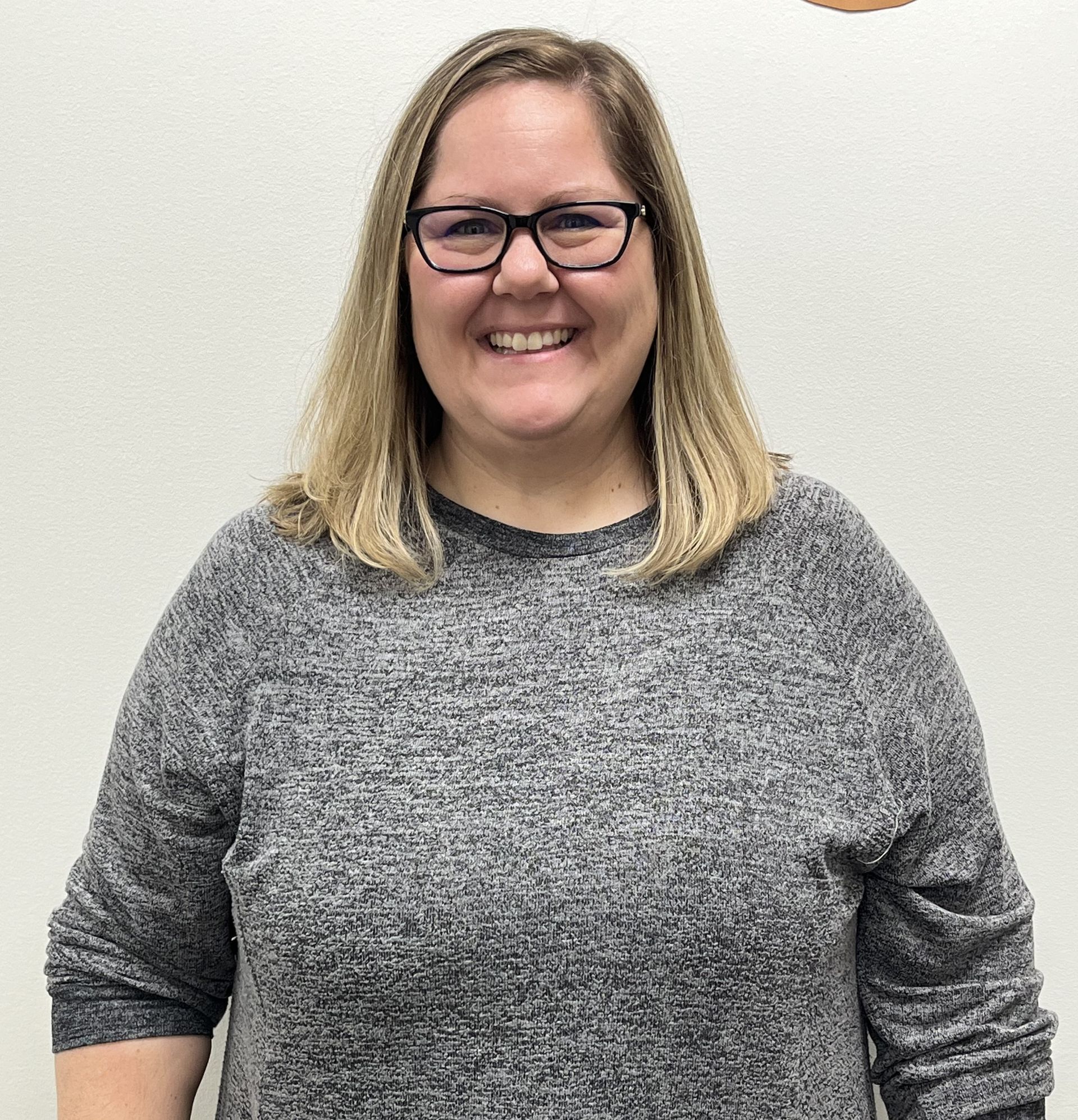 A woman wearing glasses and a grey sweater is smiling for the camera. This is Diana good.