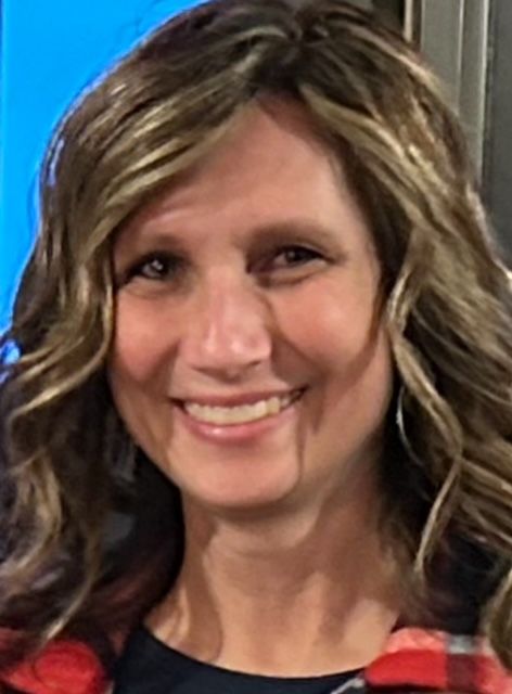 A woman in a plaid shirt is smiling for the camera.. This is Beth Homan.