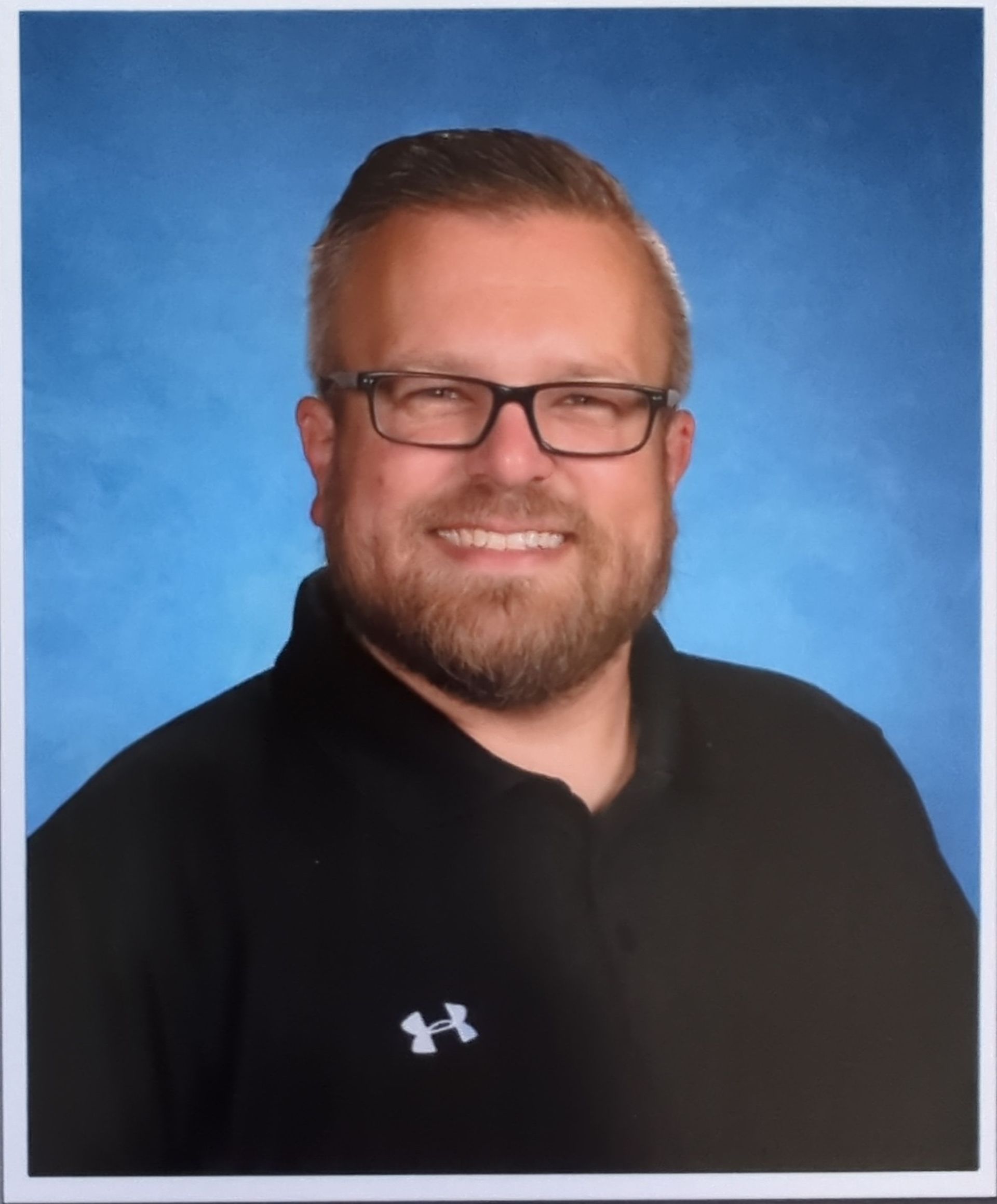A man with glasses and a beard is wearing a black under armour shirt.