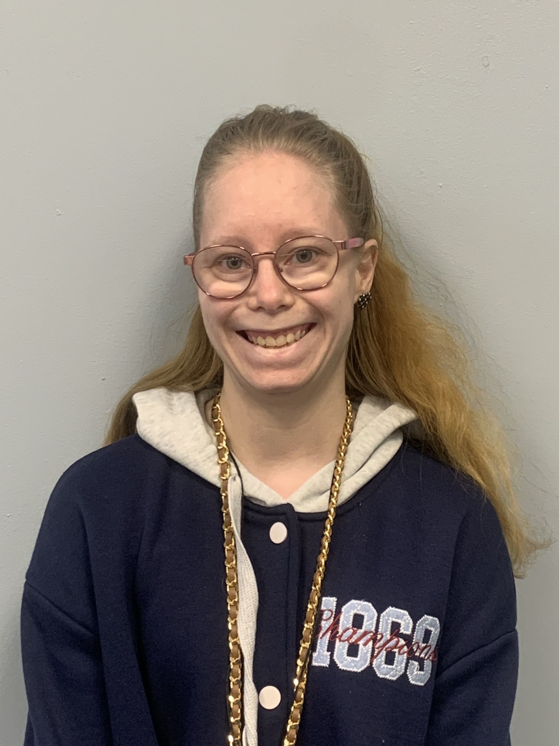 A young woman wearing glasses and a sweatshirt with the year 1969 on it is smiling.