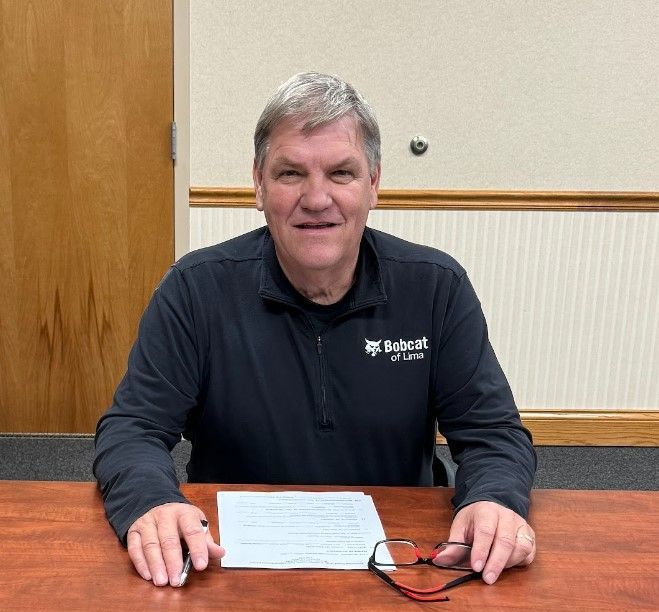 A man is sitting at a table with a piece of paper and glasses. This is Dave Shephard.