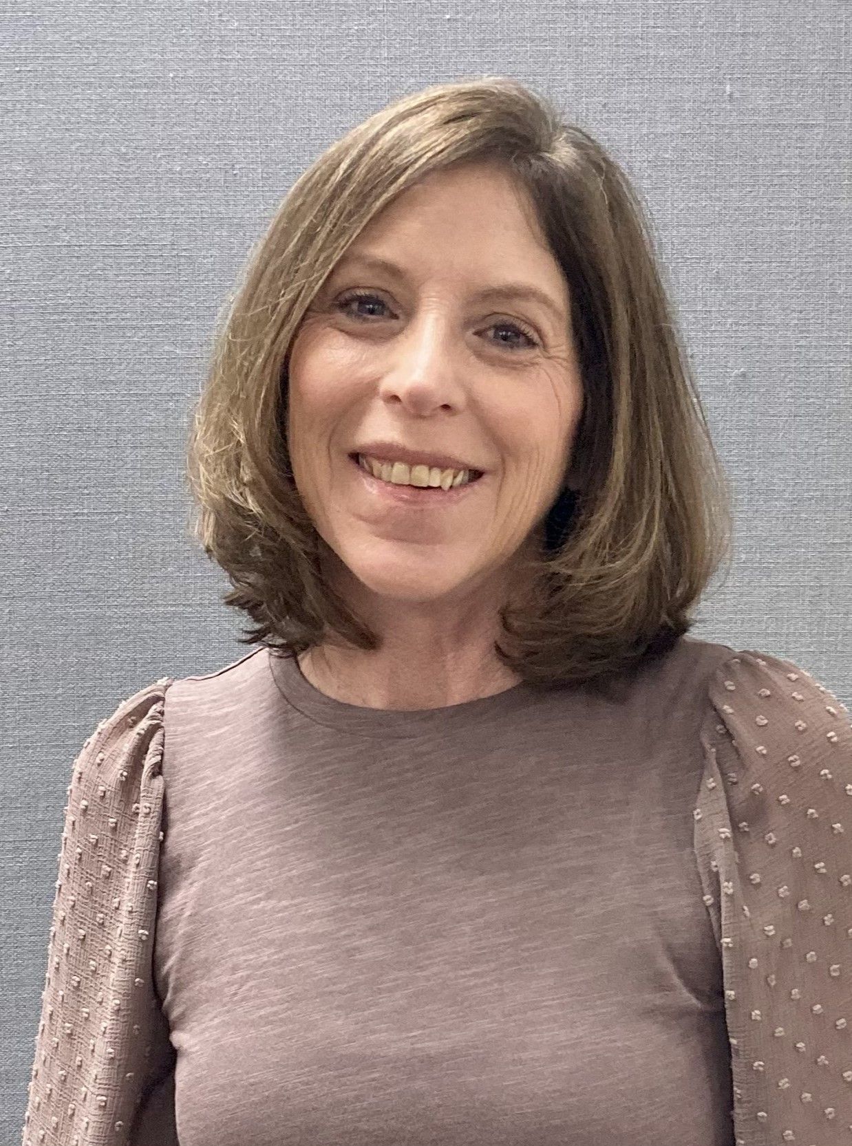 A woman in a brown shirt is smiling for the camera.