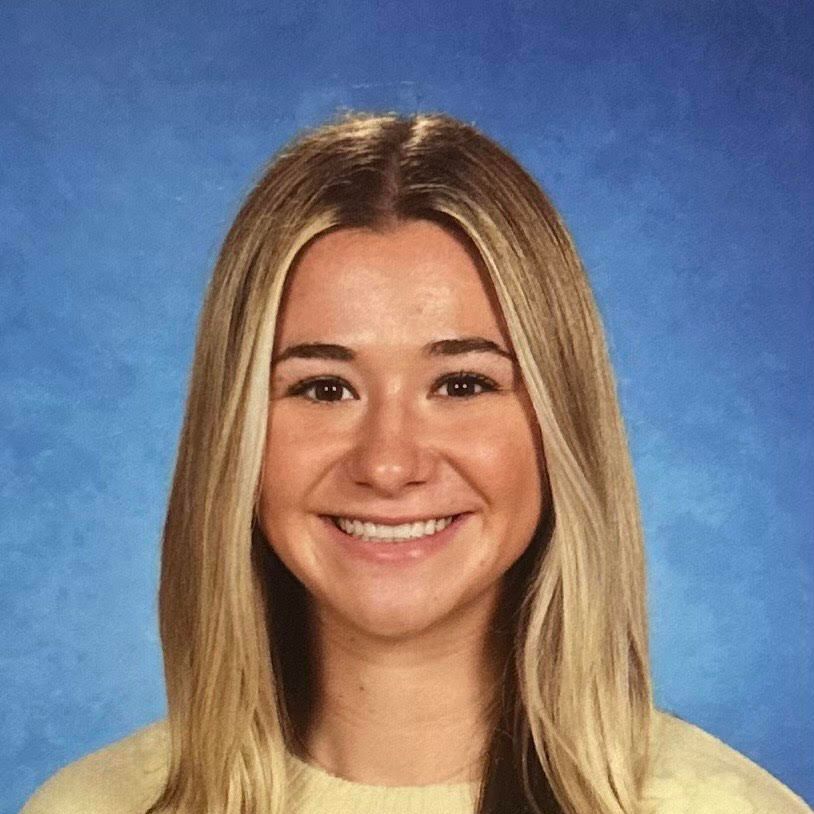 A young woman is smiling for a picture in front of a blue background.