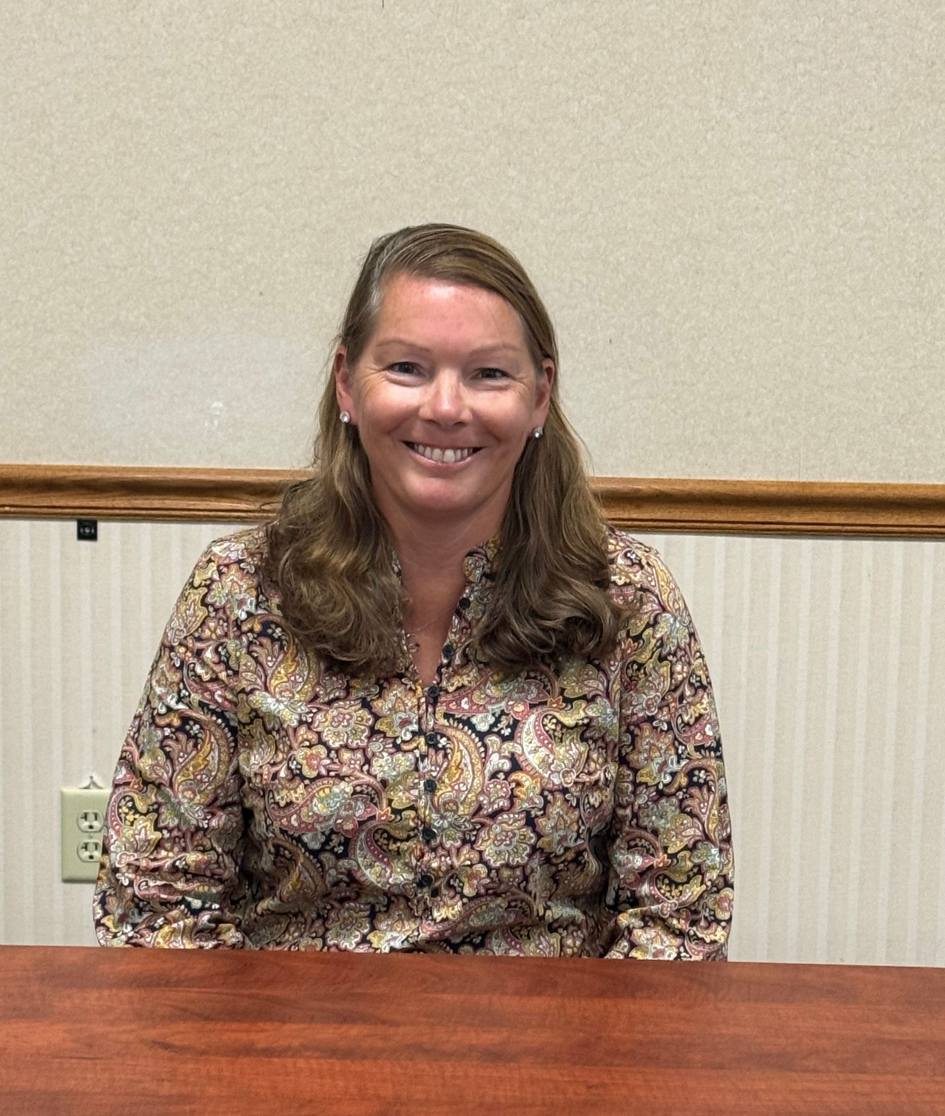 A woman is sitting at a table smiling for the camera. This is Holly Turner. 