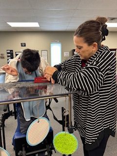 A woman in a striped shirt is standing next to a man in a wheelchair.