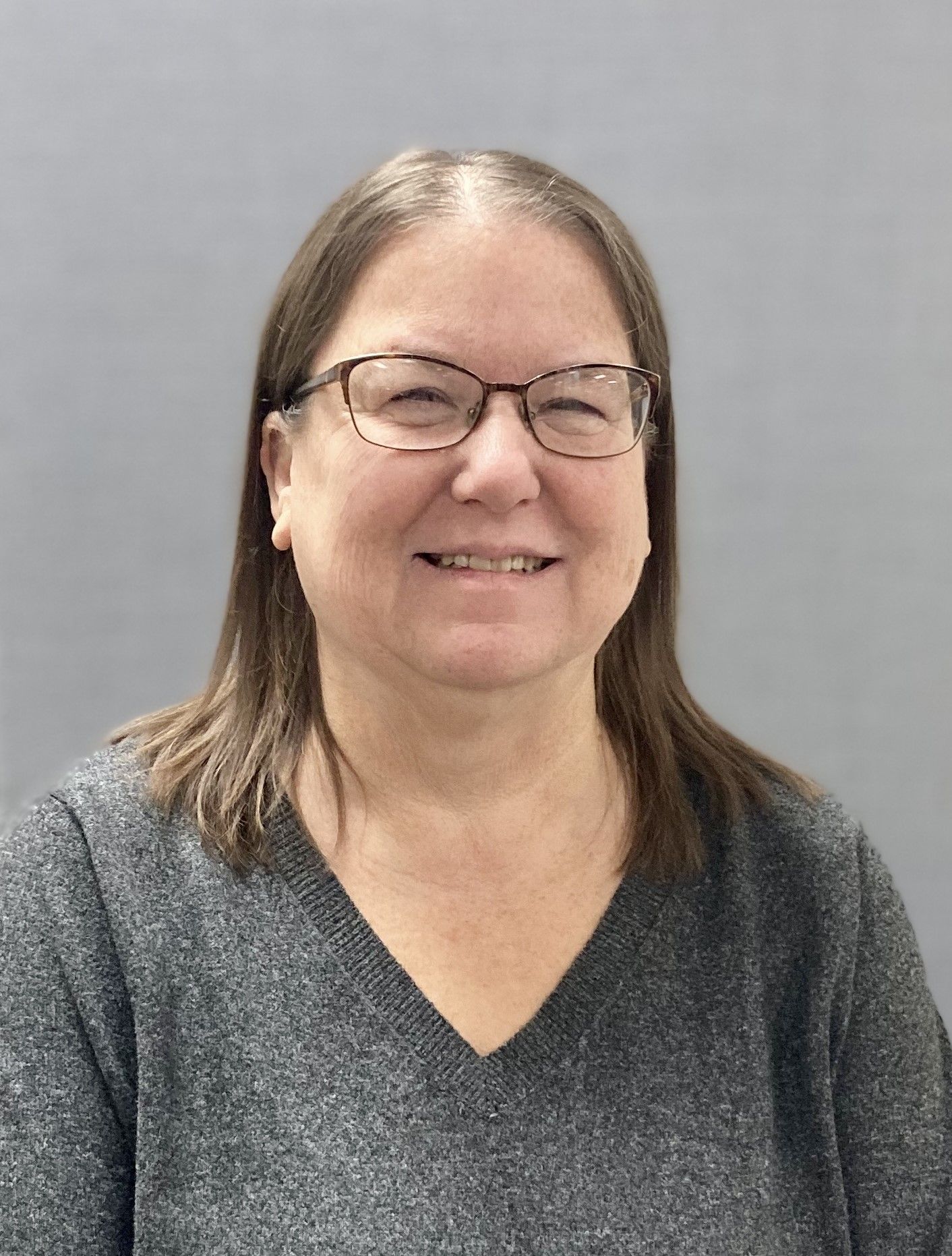 A woman wearing glasses and a grey sweater is smiling for the camera.