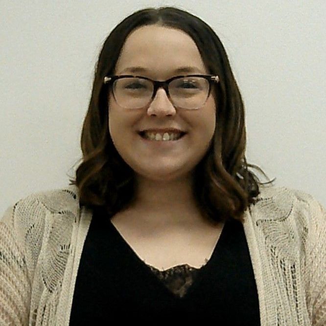 A woman wearing glasses and a sweater smiles for the camera