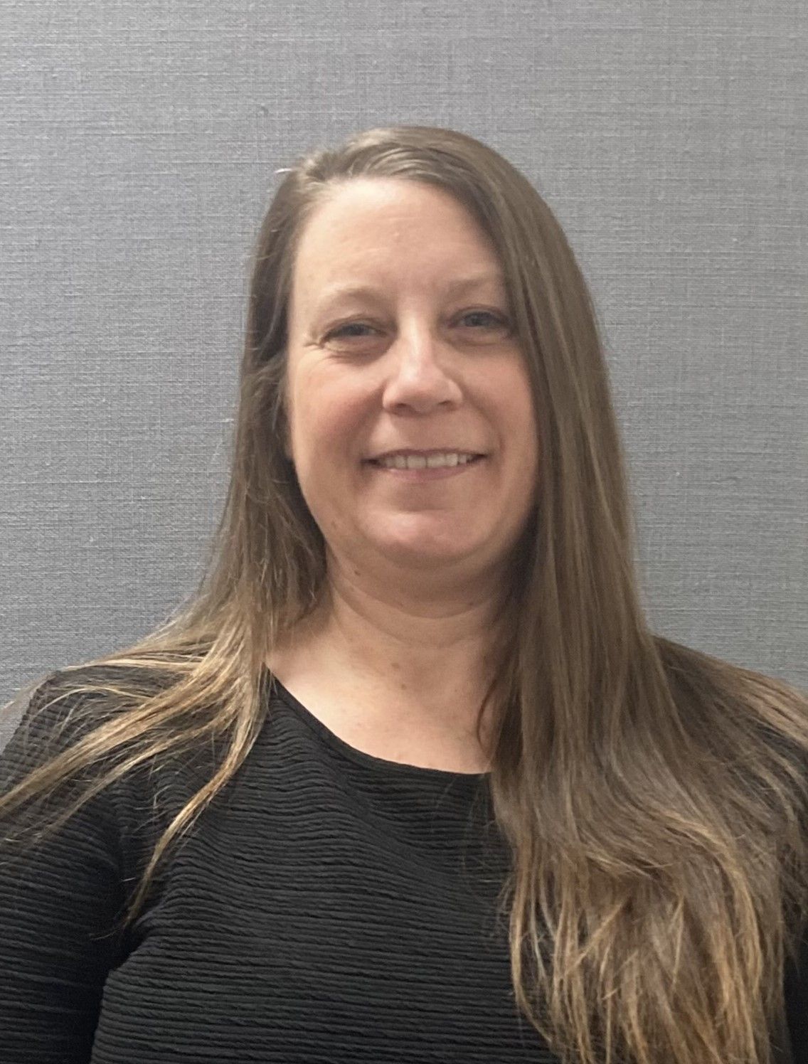 A woman with long hair is wearing a black shirt and smiling for the camera.