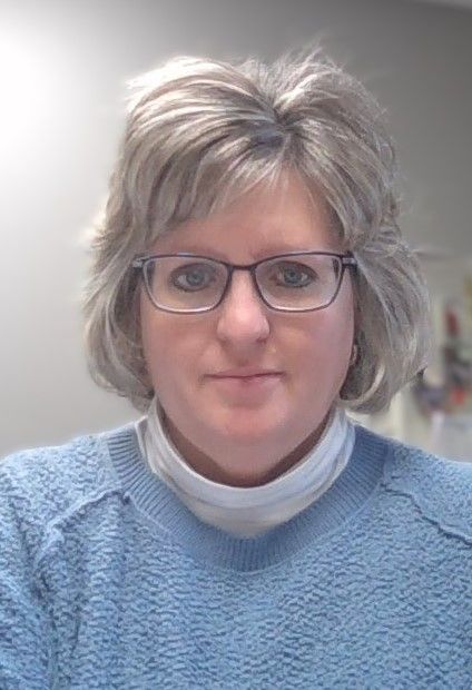 A woman wearing glasses and a blue sweater is taking a selfie.