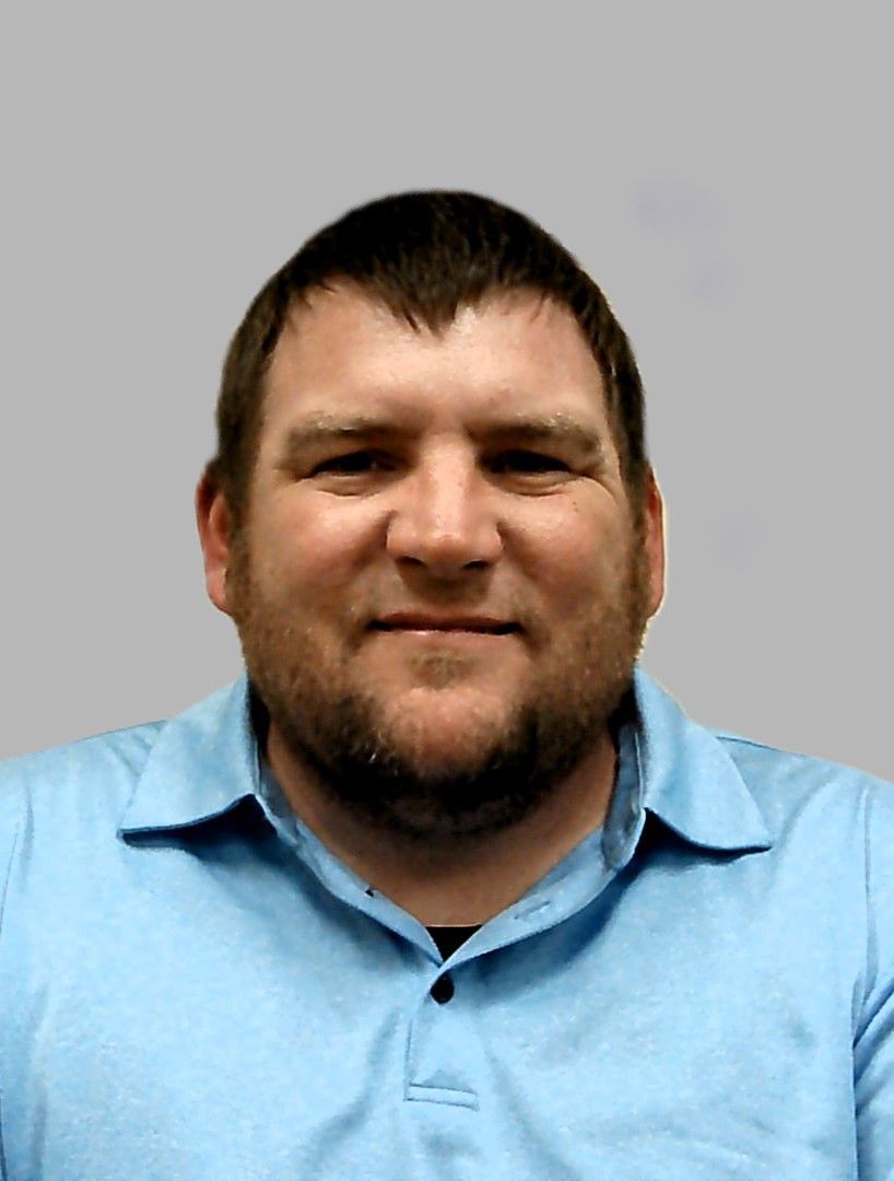 A man with a beard is wearing a blue shirt and smiling.