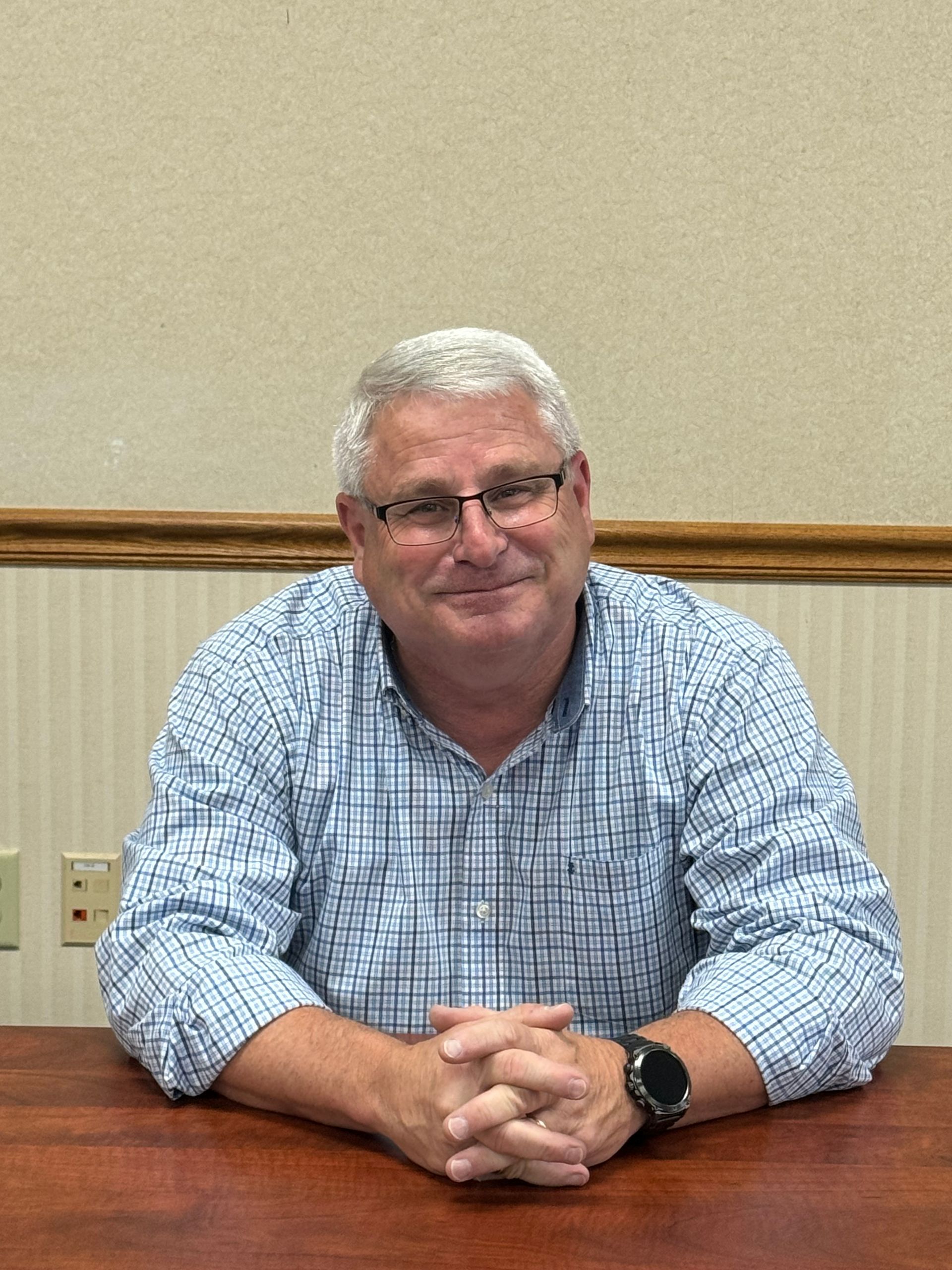 A man in a plaid shirt and glasses is sitting at a table with his hands folded. This is Mark Francis. 