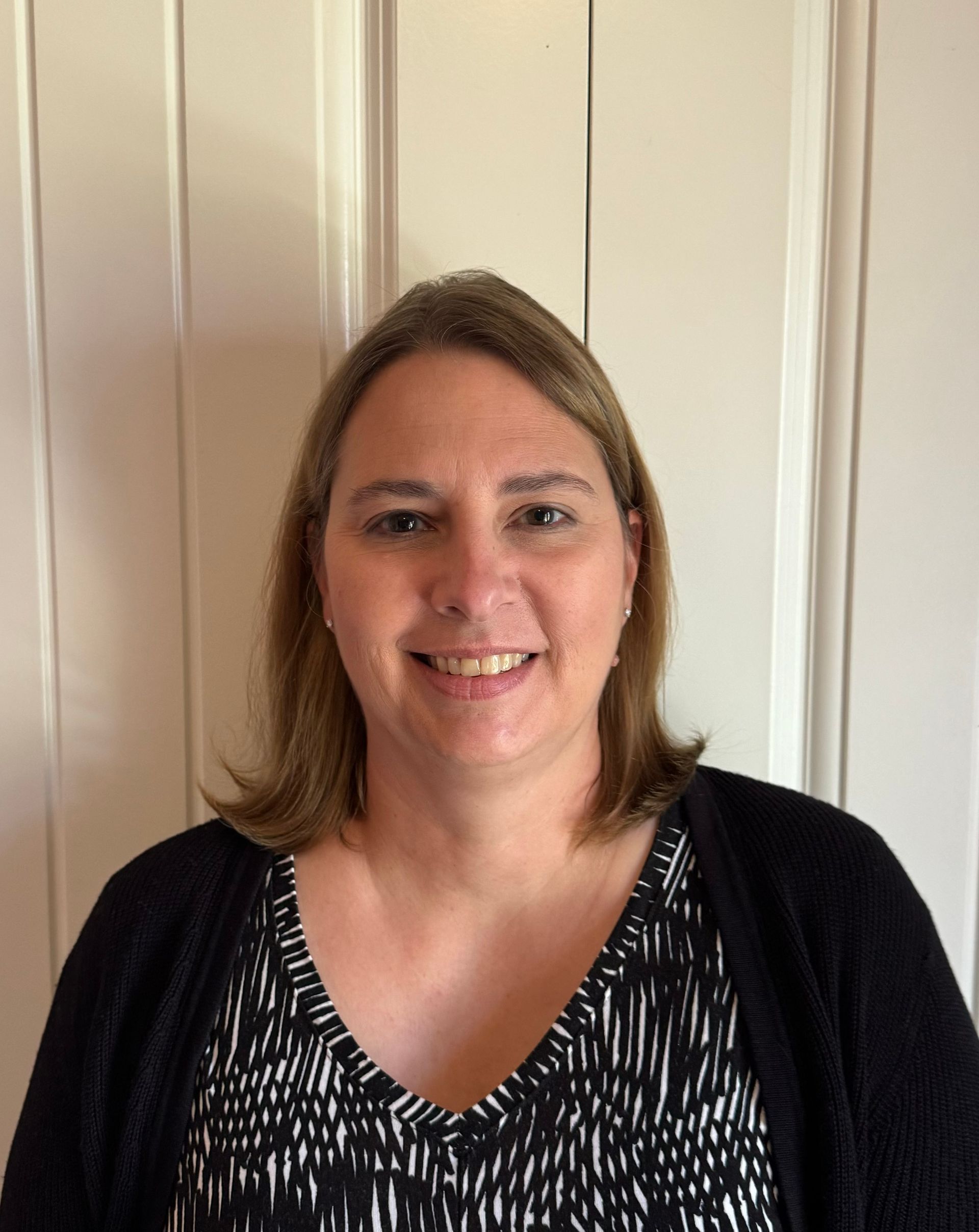 A woman wearing a black sweater and a black and white shirt is smiling for the camera.