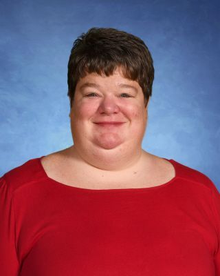 A woman in a red shirt is smiling in front of a blue background.This is Megan Miller.