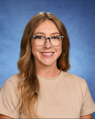 A woman wearing glasses and a tan shirt is smiling for the camera.