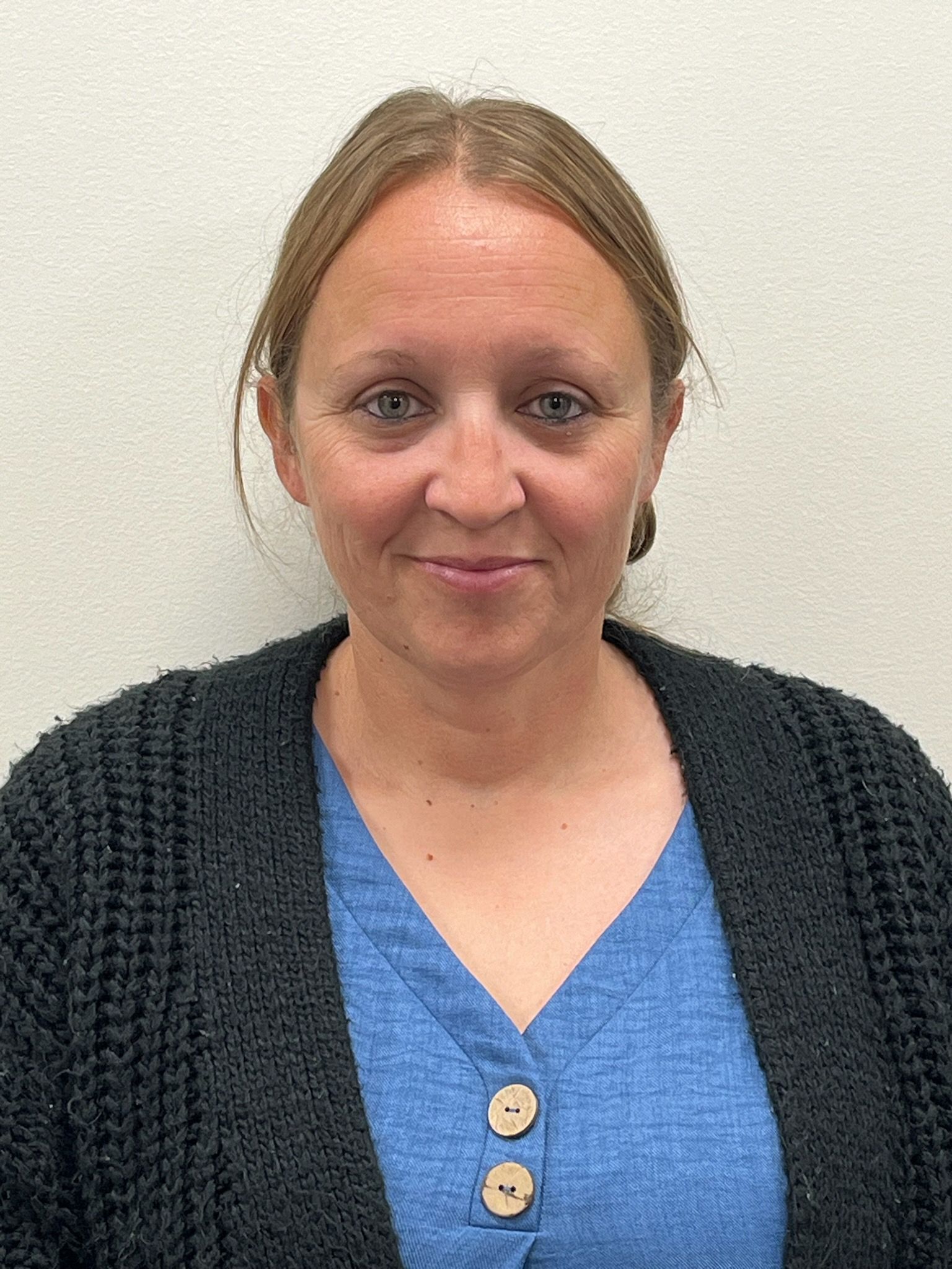 A woman wearing a blue shirt and a black sweater is smiling for the camera.