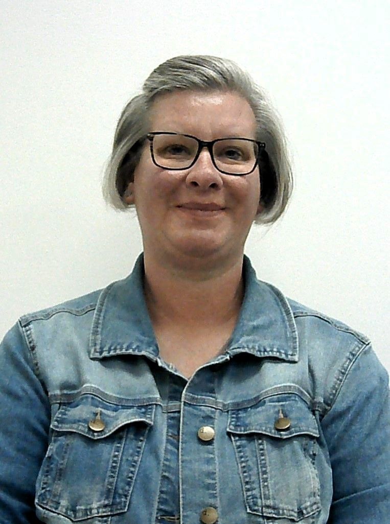 A woman wearing glasses and a denim jacket is smiling for the camera.