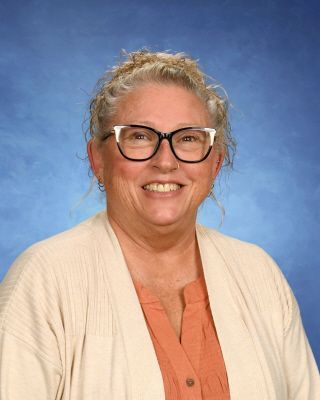 A woman wearing glasses and a sweater is smiling for a picture.
