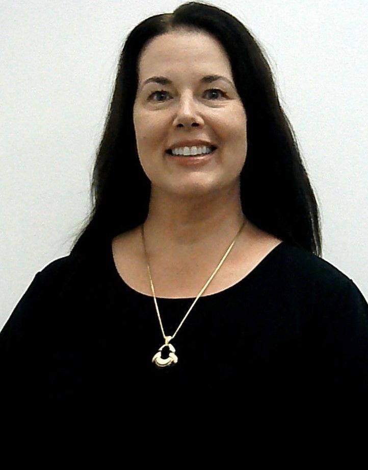 A woman wearing a black shirt and a gold necklace smiles for the camera