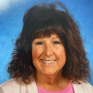 A woman with long hair and a pink shirt is smiling for a picture.