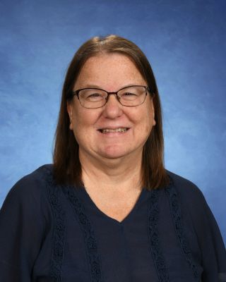 A woman wearing glasses and a grey sweater is smiling for the camera.