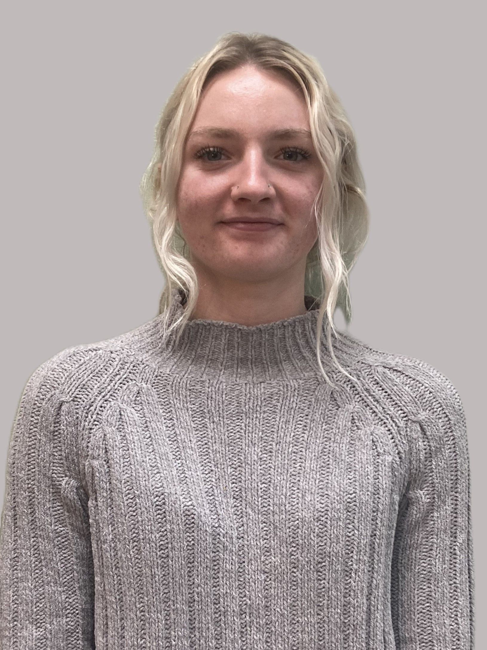 A woman is wearing a grey sweater and smiling for the camera.