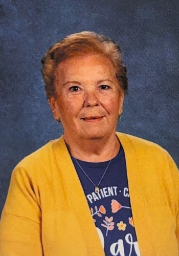 A woman wearing a yellow cardigan and a blue shirt poses for her headshot. This is Virginia McMullen.