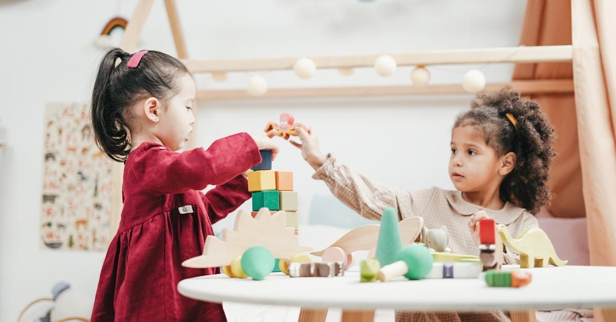Two little girls are playing with wooden blocks at a table.