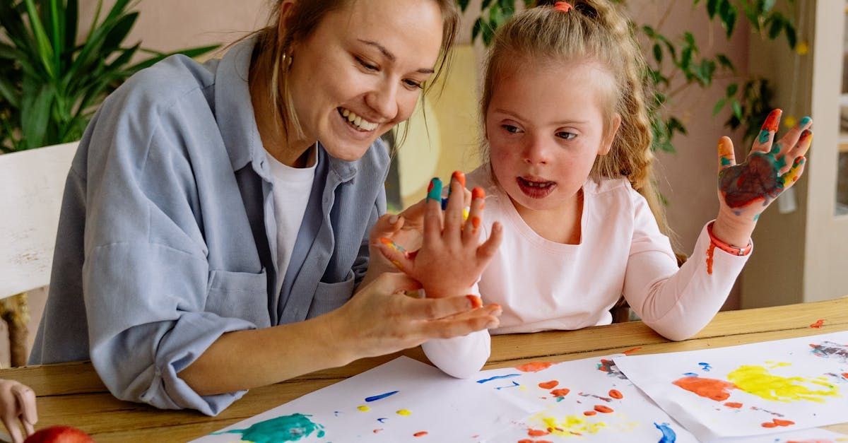 A woman and a little girl are sitting at a table with paint on their hands.